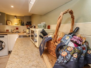 A kitchen countertop with a basket of food items a microwave kettle and a washing machine at Runnymede in Tewkesbury