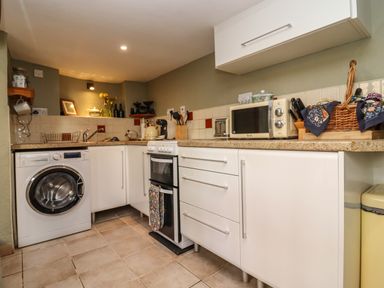 A kitchen with white cabinets a washing machine an oven countertop appliances and a basket on the counter at Runnymede in Tewkesbury
