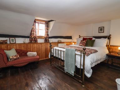 A bedroom with a brass bed frame green and patterned pillows a red patterned chaise lounge and wooden paneling at Runnymede in Tewkesbury
