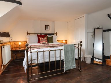 A bedroom with a metal bed frame pillows bedside tables lamps a full length mirror and wooden flooring at Runnymede in Tewkesbury