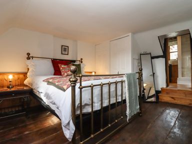 A bedroom with a brass bed frame and colorful pillows beside wooden nightstands and a full length mirror at Runnymede in Tewkesbury