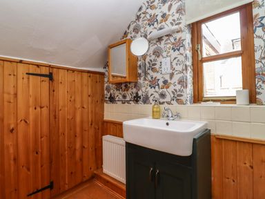 A bathroom with a sink vanity mirror window and floral wallpaper at Runnymede in Tewkesbury