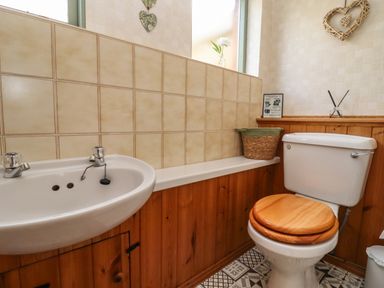 A bathroom with a sink a toilet with wooden seat and a woven basket on a shelf at Runnymede in Tewkesbury