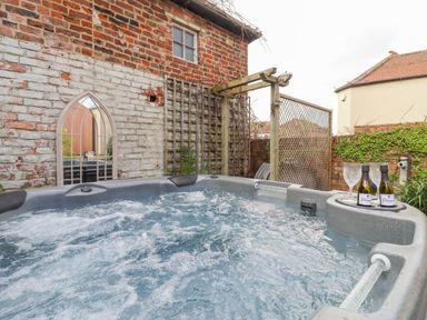 An outdoor hot tub with bubbling water next to a brick wall with a mirror and a wooden trellis at Runnymede in Tewkesbury