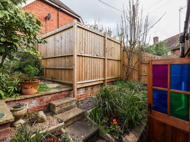 A garden area with stone steps leading up to a wooden fence and plants in pots and garden beds at Runnymede in Tewkesbury