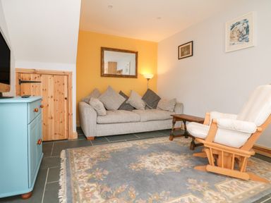 A living room with a sofa, armchair, wooden chest, wall mirror, and a lamp at Hill Coach House in Watchet