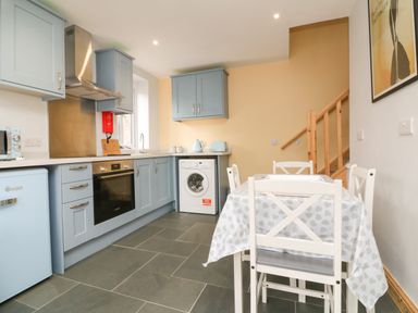 A kitchen with blue cabinets a washing machine and a dining table with chairs at Hill Coach House in Watchet