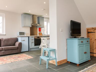 A living room and kitchen area with a brown sofa a blue fridge blue cabinets and a blue TV stand at Hill Coach House in Watchet