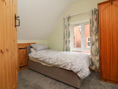 A small bedroom with a single bed next to a window with patterned curtains and wooden wardrobes at Hill Coach House Watchet