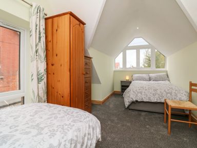 A bedroom with two beds a wooden wardrobe chest of drawers bedside table with lamp chair and windows at Hill Coach House in Watchet