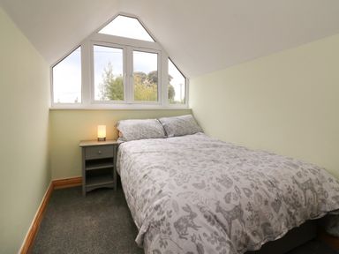 A small bedroom with a bed and a bedside table with a lamp under a sloped ceiling at Hill Coach House in Watchet