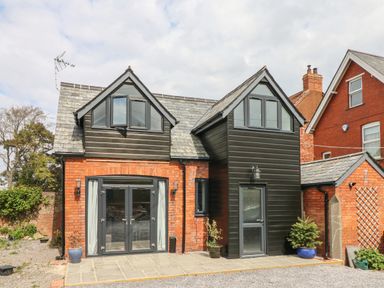 A brick house with black wooden upper gables and multiple windows with a stone tiled patio in front at Hill Coach House in Watchet
