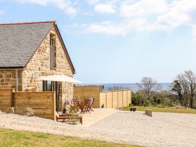 A stone house with a wooden fence patio furniture and a view of trees and the sea at Apple Blossom Barn in Gulval near Penzance