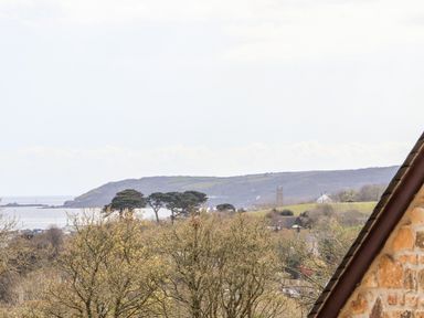 A landscape view with trees hills and a coastline next to a stone building at Apple Blossom Barn in Gulval near Penzance