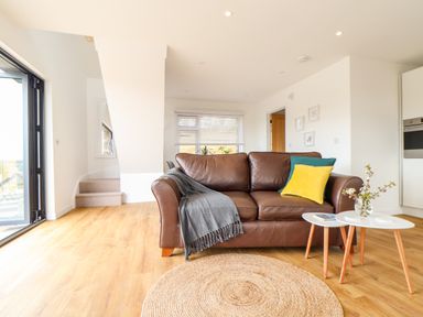 A living room with a brown leather sofa and small white tables with flowers at Apple Blossom Barn in Gulval near Penzance