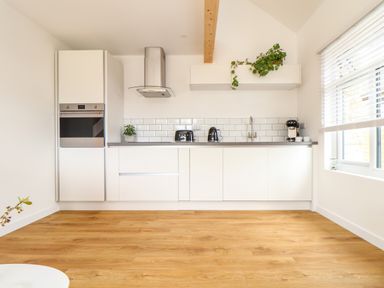 A kitchen with white cabinets stainless steel appliances a plant on the counter and a window with blinds at Apple Blossom Barn in Gulval near Penzance
