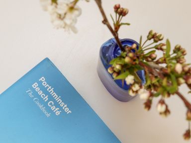 A blue cookbook and a branch with buds in a blue vase on a white surface at Apple Blossom Barn in Gulval near Penzance