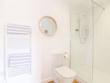 A bathroom with a toilet a circular mirror a towel rack with striped towels and a shower at Apple Blossom Barn in Gulval near Penzance