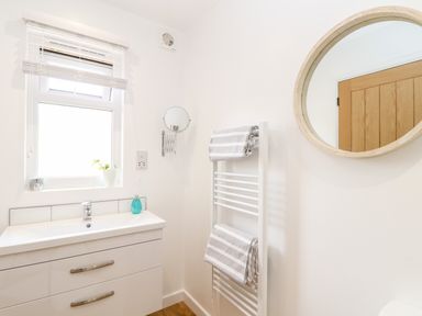 A bathroom with a vanity sink under a window next to a towel rack with towels and a round mirror at Apple Blossom Barn in Gulval near Penzance