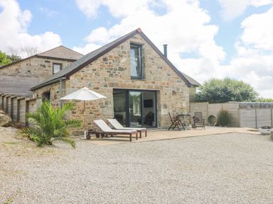 A stone house with a patio featuring two lounge chairs and an umbrella and a table with chairs at Apple Blossom Barn in Gulval near Penzance