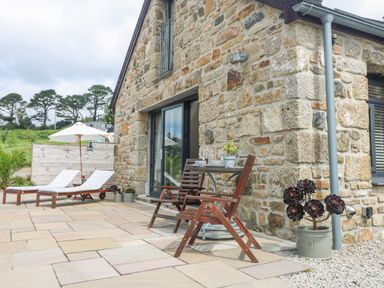 An outdoor patio with two wooden chairs and a small table beside a stone house at Apple Blossom Barn in Gulval near Penzance