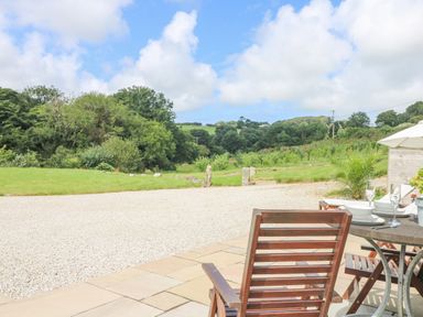 A patio with wooden chairs and a table set for dining overlooking a gravel area and green fields at Apple Blossom Barn in Gulval near Penzance