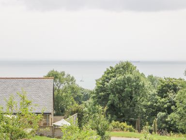 View of trees sea and a roof with sailboats on water at Apple Blossom Barn in Gulval near Penzance