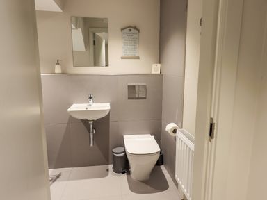 A bathroom with a wall-mounted sink, a toilet, a mirror, a radiator, and a trash bin at Rivers Edge in Newby Bridge