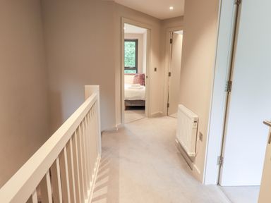A hallway with a white railing radiator and open doors showing a bedroom at Rivers Edge in Newby Bridge