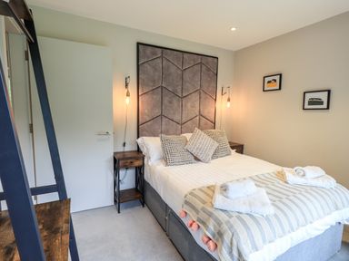 A bedroom with a bed with pillows and folded towels on it two wall lamps and framed pictures on the wall at Rivers Edge in Newby Bridge