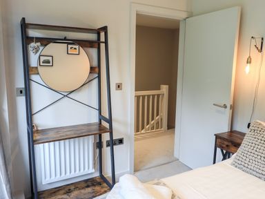 A bedroom with a wooden vanity with a round mirror and an open door showing a stair railing at Rivers Edge in Newby Bridge
