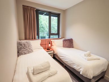 A bedroom with two single beds white bedding and folded towels near a window at Rivers Edge in Newby Bridge