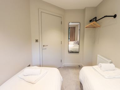 A bedroom with two single beds towels on beds a door a wall mirror and a clothes rack with hangers at Rivers Edge in Newby Bridge