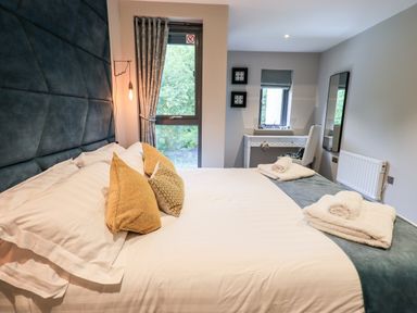 A bedroom with a large bed with pillows and folded towels a window with curtains a desk and a mirror at Rivers Edge in Newby Bridge