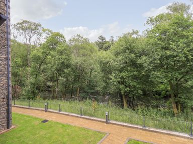 A view of a riverside with green trees and a stone building on the left at Rivers Edge in Newby Bridge