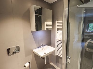 A bathroom with a wall-mounted sink cabinet towel rail and glass shower door at Rivers Edge Newby Bridge