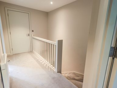 A hallway with carpeted floor a white door and a staircase with a white railing at Rivers Edge in Newby Bridge