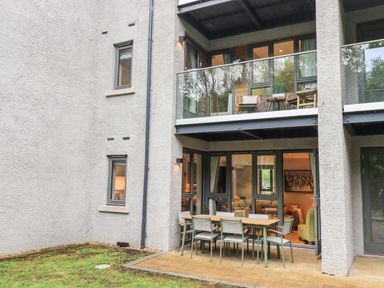 An outdoor patio dining set with six chairs and a table outside a ground floor apartment with glass balcony above at Rivers Edge in Newby Bridge