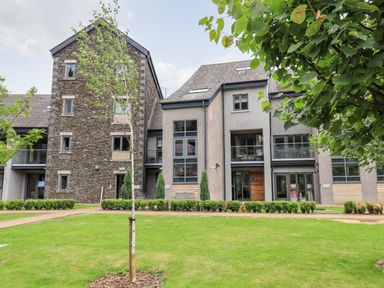 Exterior view of a modern residential building with stone and plaster walls and glass balconies at Rivers Edge in Newby Bridge