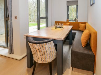A dining area with a wooden table cushioned bench seating and a fabric chair at Rivers Edge in Newby Bridge