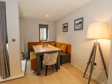A dining nook with a wooden table a yellow and gray bench and a patterned chair next to a floor lamp and two framed pictures at Rivers Edge in Newby Bridge