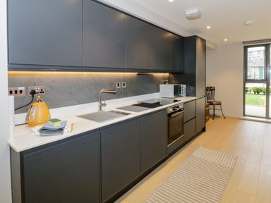 A kitchen with dark cabinets a sink yellow kettle microwave oven and a chair near a glass door at Rivers Edge in Newby Bridge