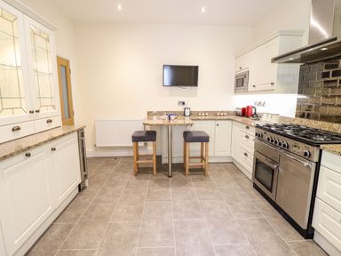 A kitchen with white cabinets a stainless steel stove two stools and a wall mounted television at Craigside in Betws-Y-Coed