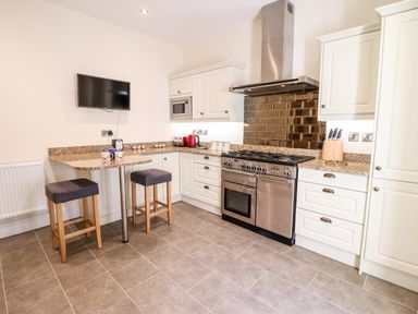 A kitchen with a stove microwave two stools and a wall mounted television at Craigside in Betws-Y-Coed