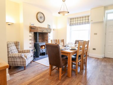 A dining room with a wooden table and chairs next to a fireplace with a clock above at Craigside in Betws-Y-Coed