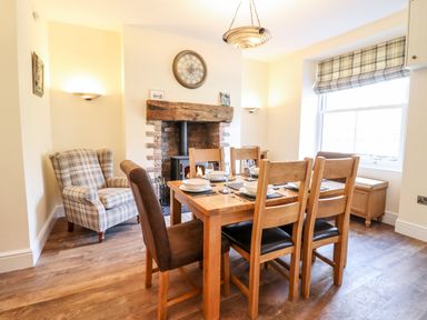 A dining room with a wooden table set for six near a brick fireplace and an armchair at Craigside in Betws-Y-Coed