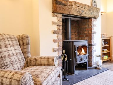 A plaid armchair next to a wood-burning stove in a brick fireplace at Craigside Betws-Y-Coed