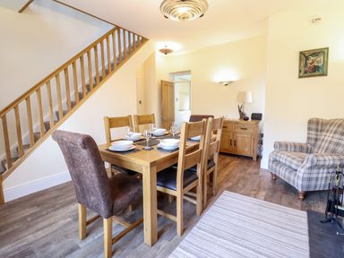 A dining area with wooden table set for six under staircase beside an armchair and sideboard at Craigside in Betws-Y-Coed