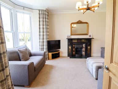A living room with sofas a striped ottoman a fireplace with a mirror above and a television at Craigside in Betws-Y-Coed