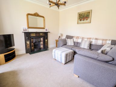 A living room with a gray sofa ottoman fireplace television and mirror at Craigside in Betws-Y-Coed